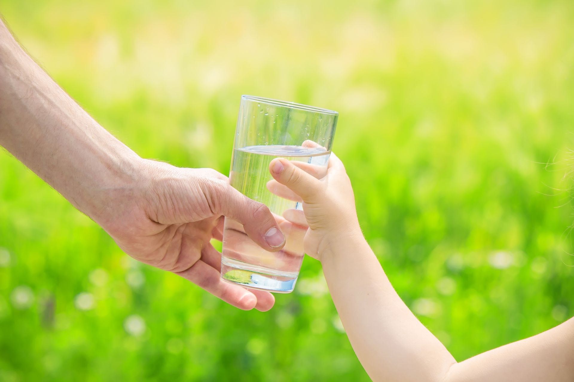 Volwassene geeft een glas water aan de hand van een kind, groene achtergrond.