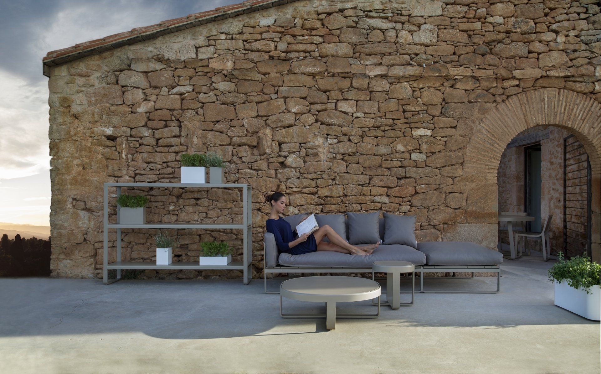 Eine Frau sitzt auf einer Couch und liest ein Buch vor einer Steinmauer