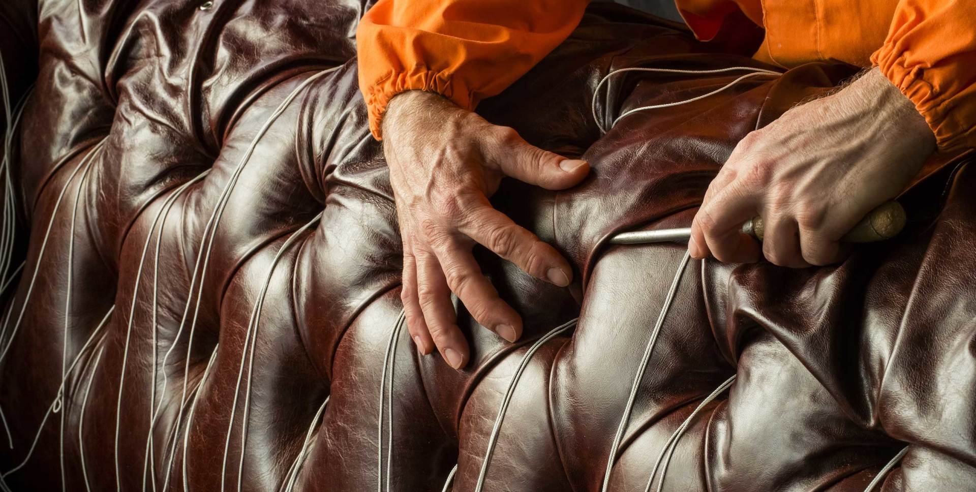 Ein Mann in einer orangefarbenen Jacke arbeitet an einem braunen Ledersofa.
