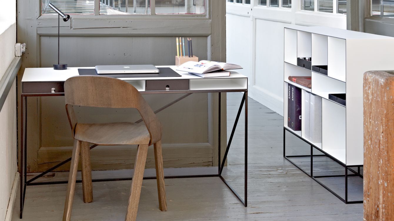 Ein Holzstuhl steht vor einem Schreibtisch mit einem Laptop darauf