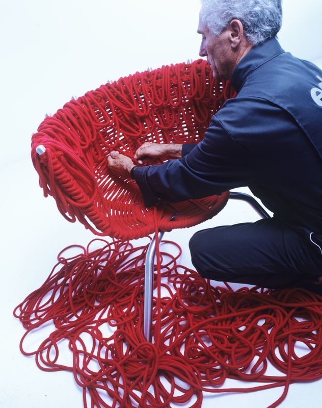 Ein Mann kniet neben einem Stuhl aus rotem Garn