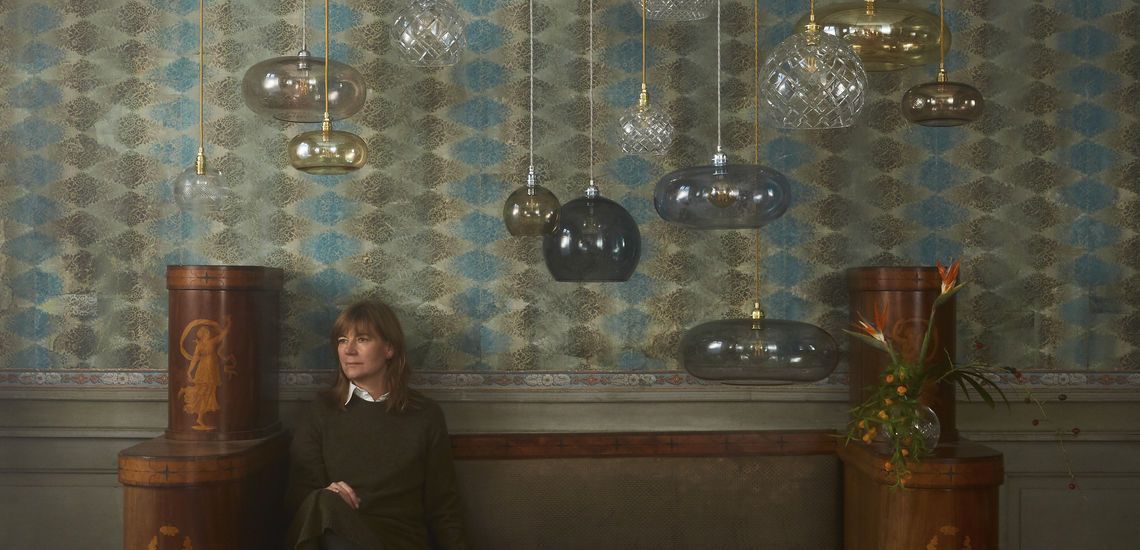 Eine Frau sitzt auf einer Couch in einem Raum, von dessen Decke viele Lampen hängen.