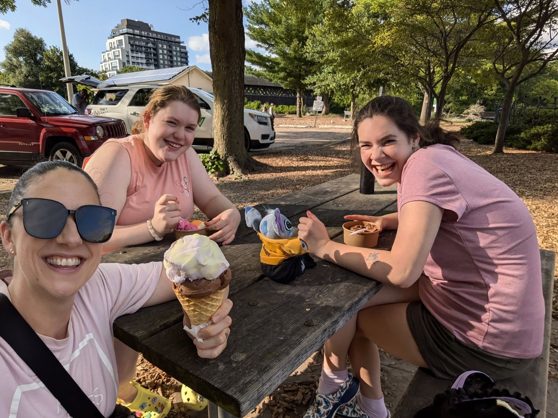Three girls smiling at a picnic table with ice cream cones, outdoors.