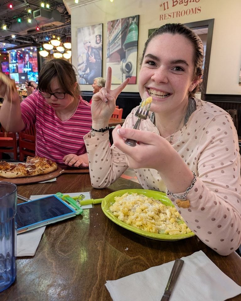 Two smiling girls eating at a restaurant. One holds a fork, the other pizza.