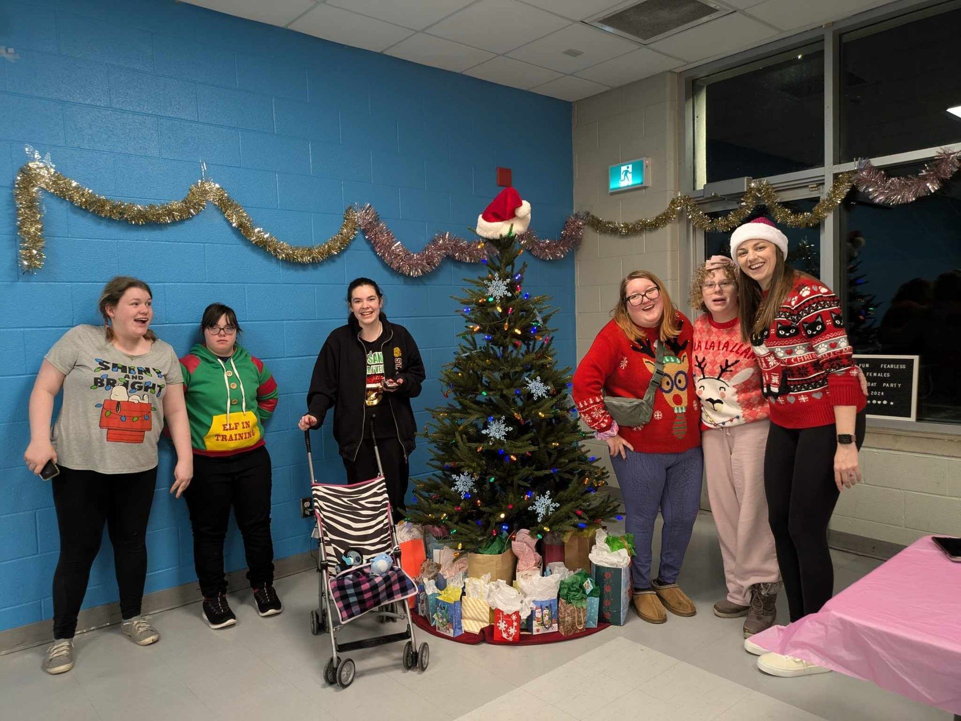 Group of girls posing by a decorated Christmas tree in a room with a blue wall.
