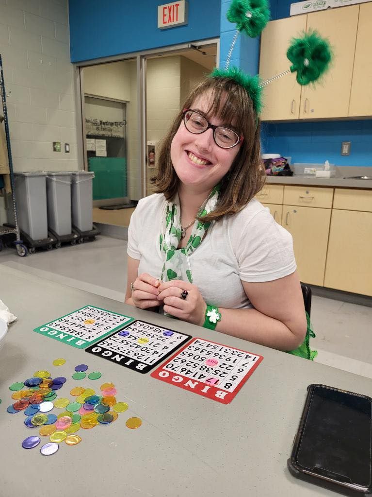 Woman wearing St. Patrick's Day decorations smiles, playing bingo at a table with cards and colorful chips.