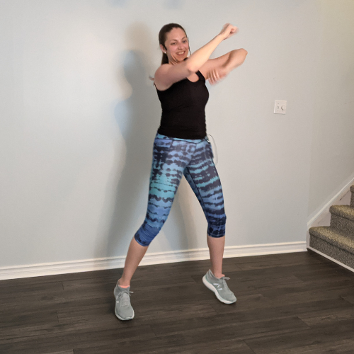 Woman in athletic wear exercising indoors, angled arm punches, smiling.