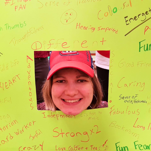 Woman in red cap, smiling, framed by a yellow board with handwritten positive adjectives.