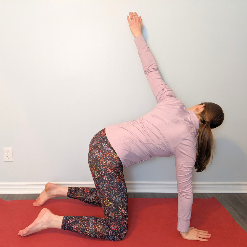 Woman in a yoga pose, left knee down, right arm reaching up, on a red mat.