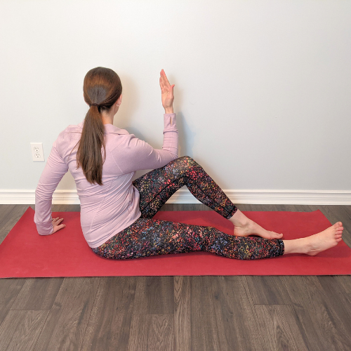Woman in seated spinal twist pose on a red yoga mat.