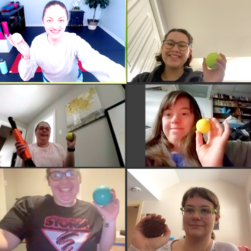 Six people on a video call hold different colored massage balls, smiling at the camera. Indoor setting.