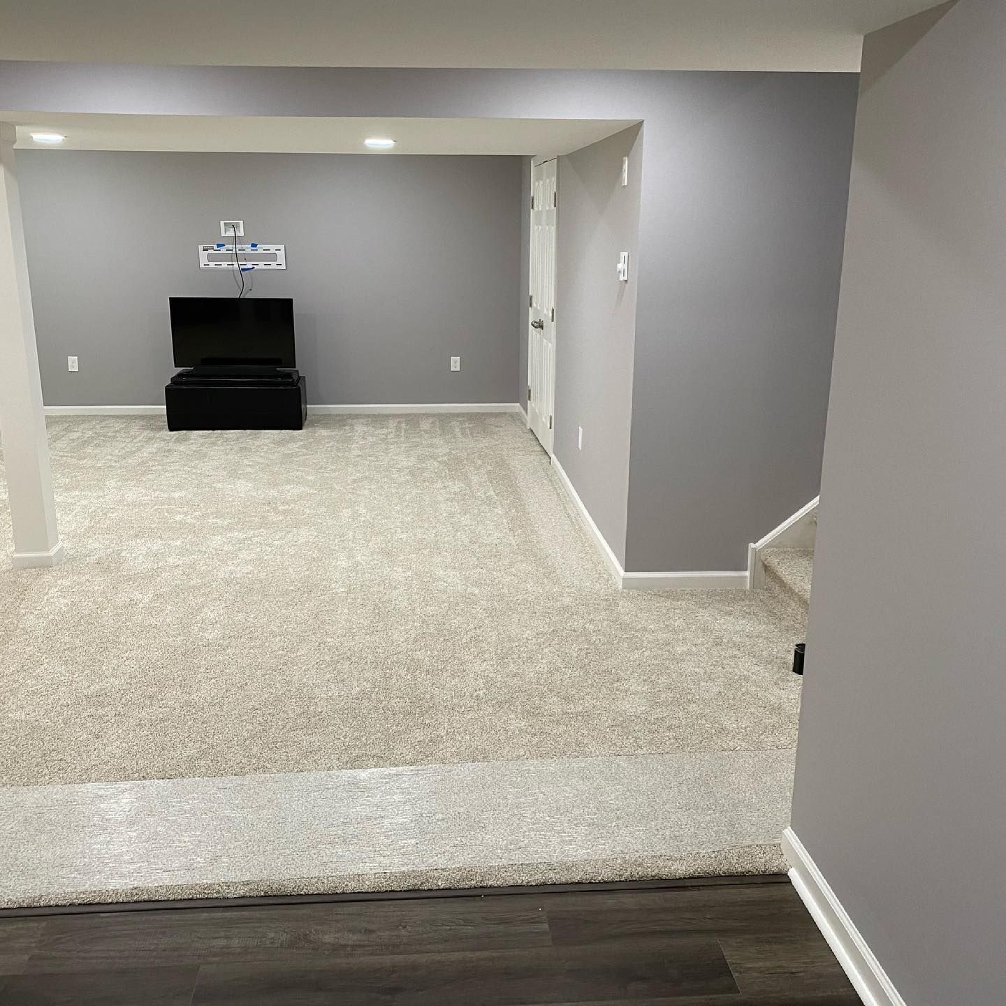 A basement with a carpeted floor and a television on the wall.