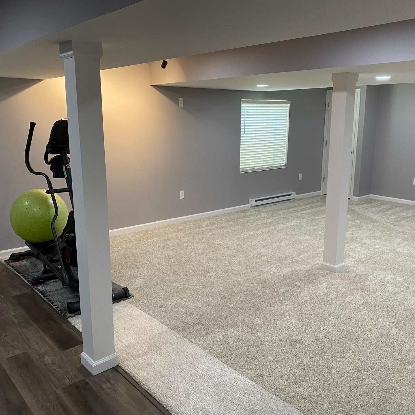 A basement with a exercise bike and a ball on the floor.