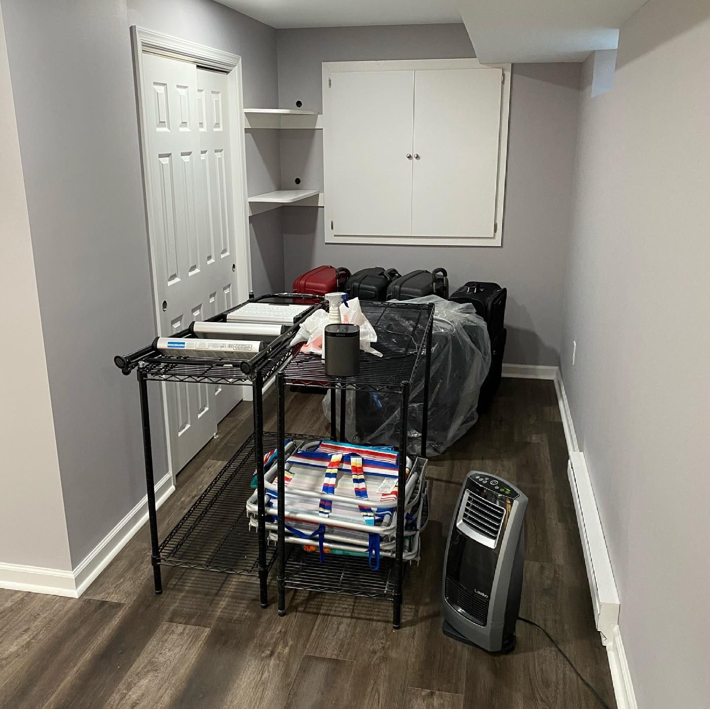 A room with a bed , a fan , a shelf , and a window.