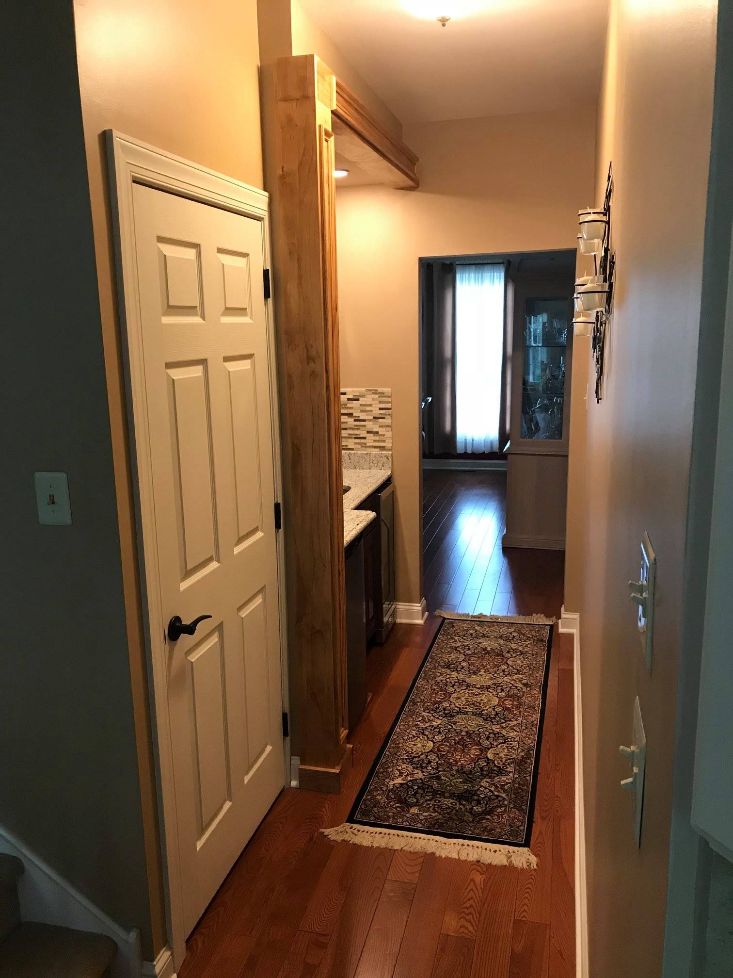 A hallway with hardwood floors and a rug leading to a living room.