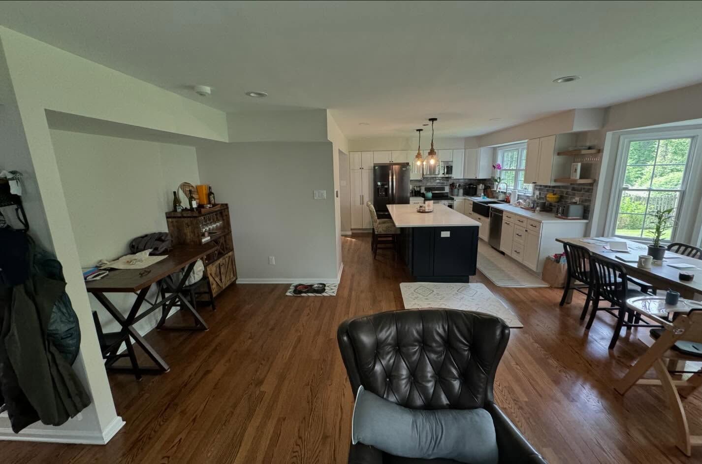 A living room with hardwood floors , a chair , a table and a kitchen.