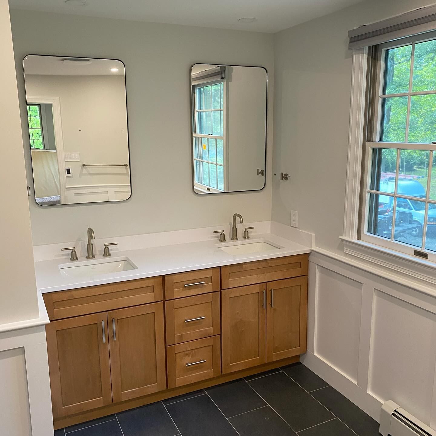A bathroom with two sinks , two mirrors and a window.