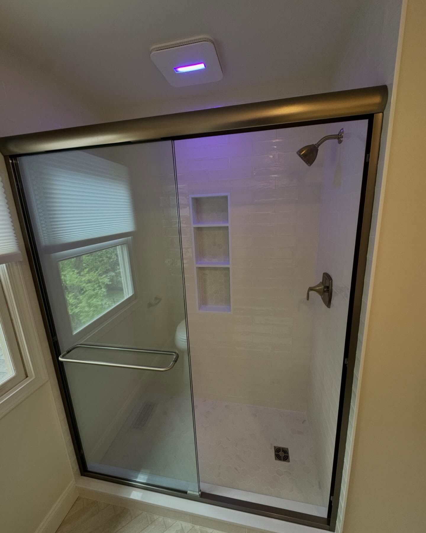 A bathroom with a sliding glass shower door and a window.