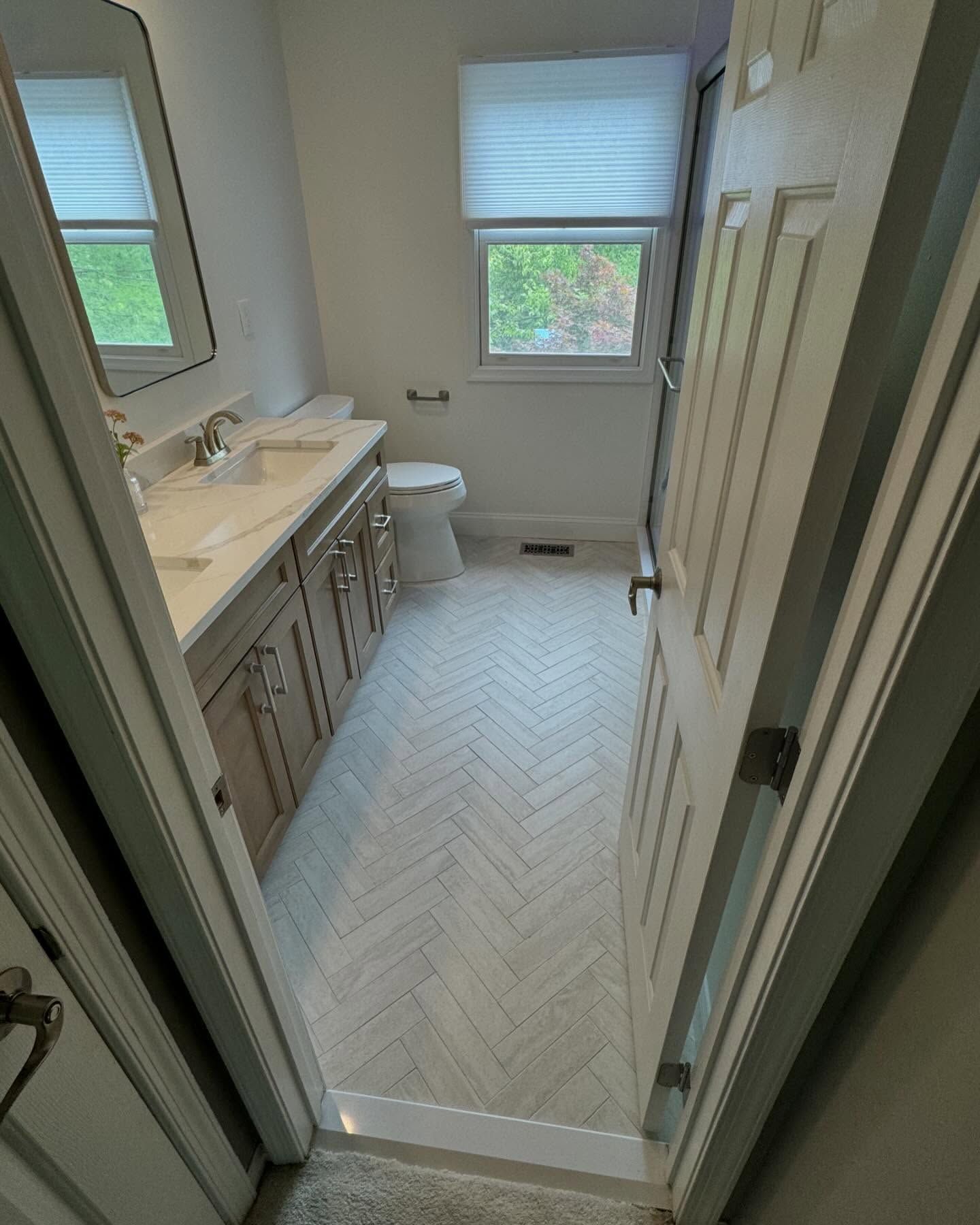 A bathroom with a sink , toilet , mirror and window.