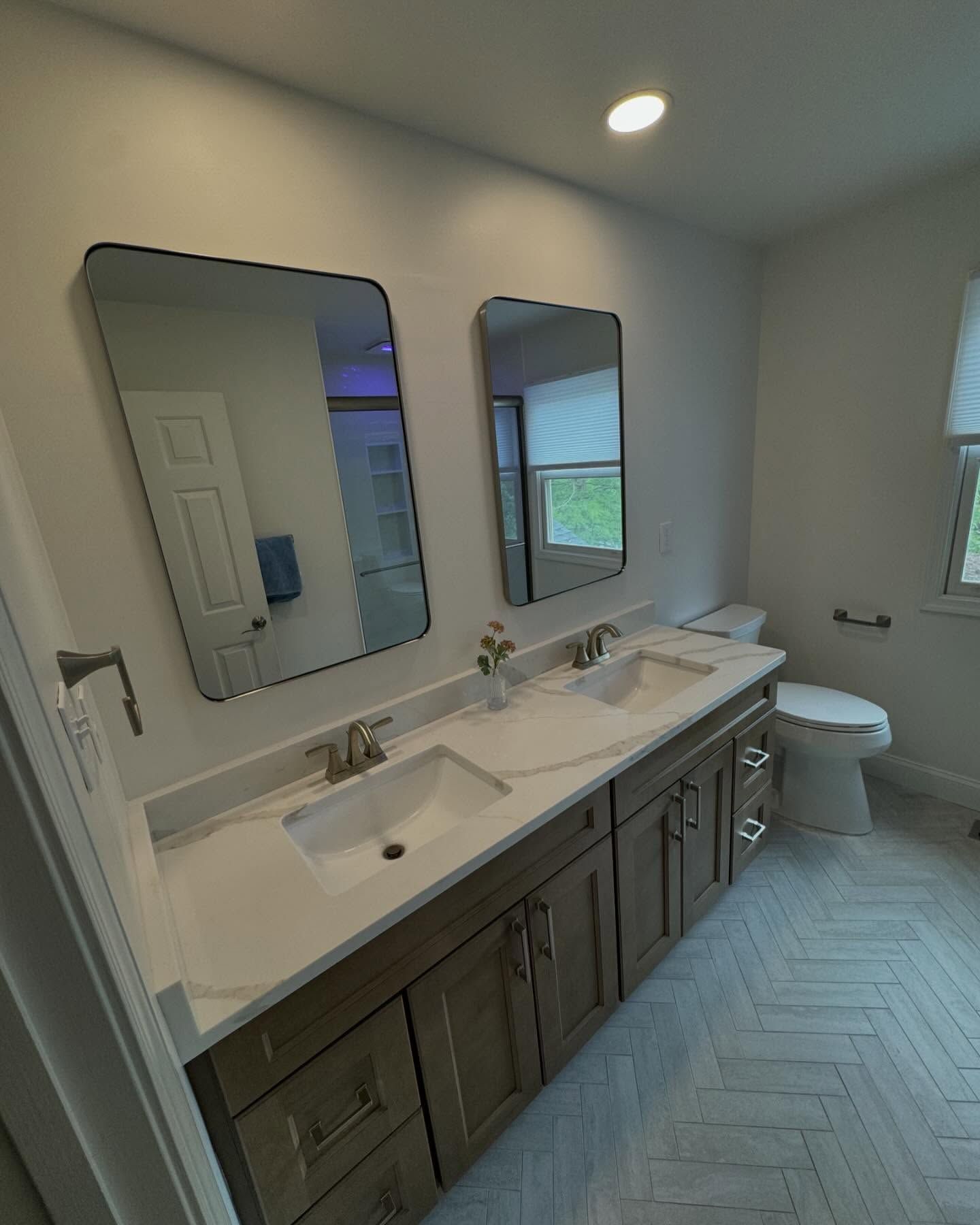 A bathroom with two sinks , two mirrors and a toilet.