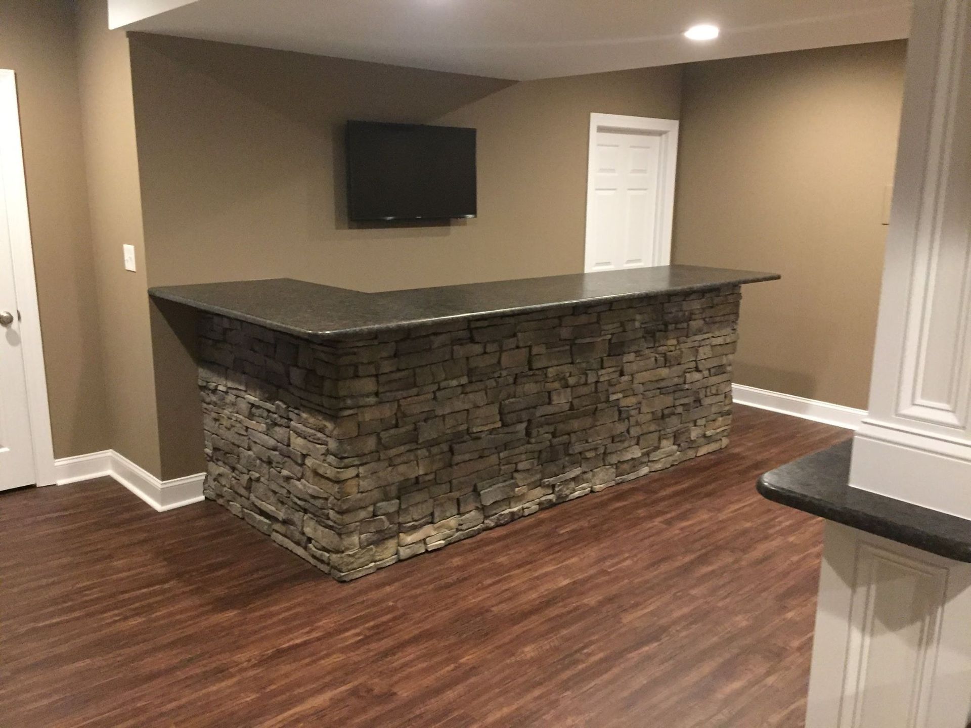 A basement with a stone bar and a flat screen tv.