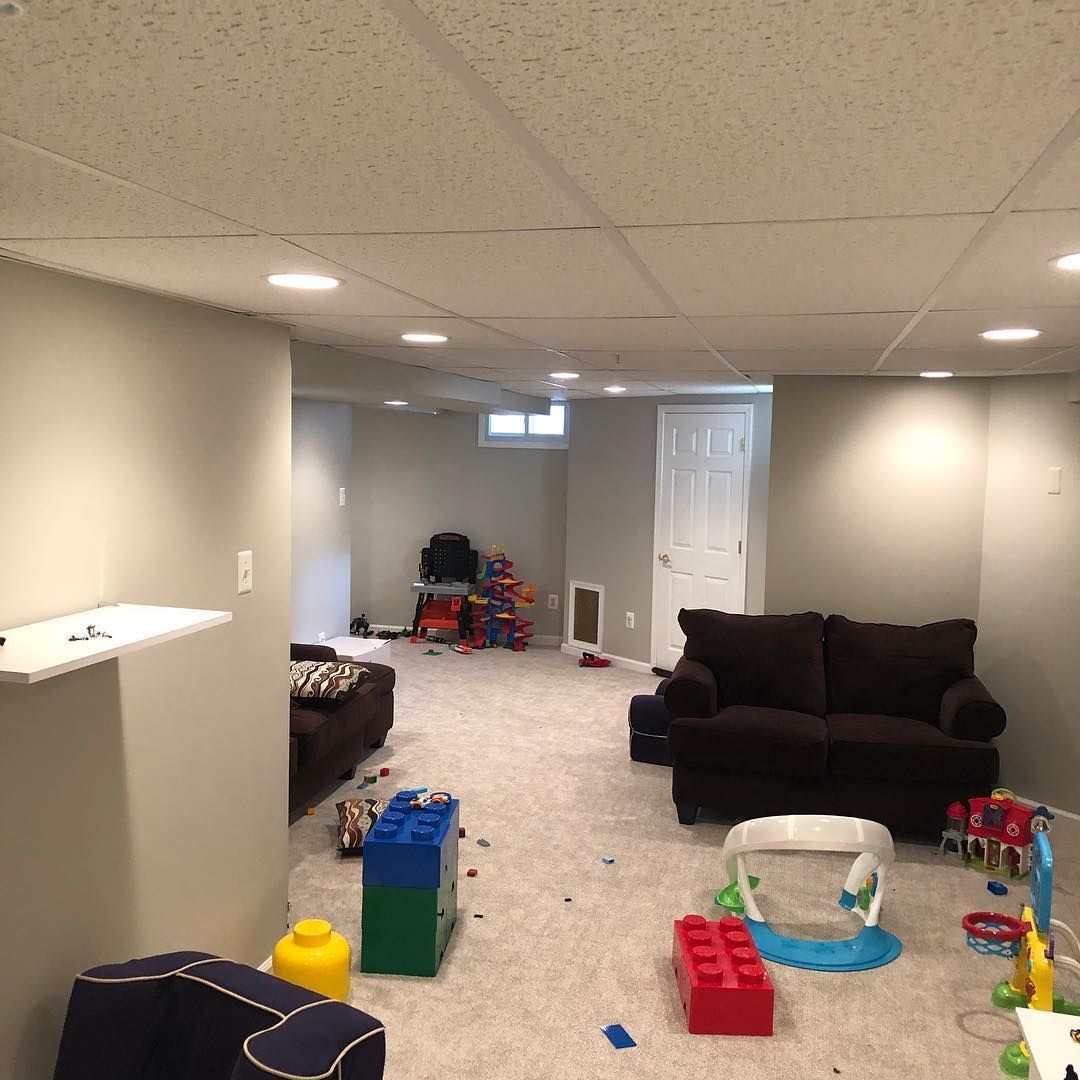 A basement with a couch , chairs , and toys on the floor