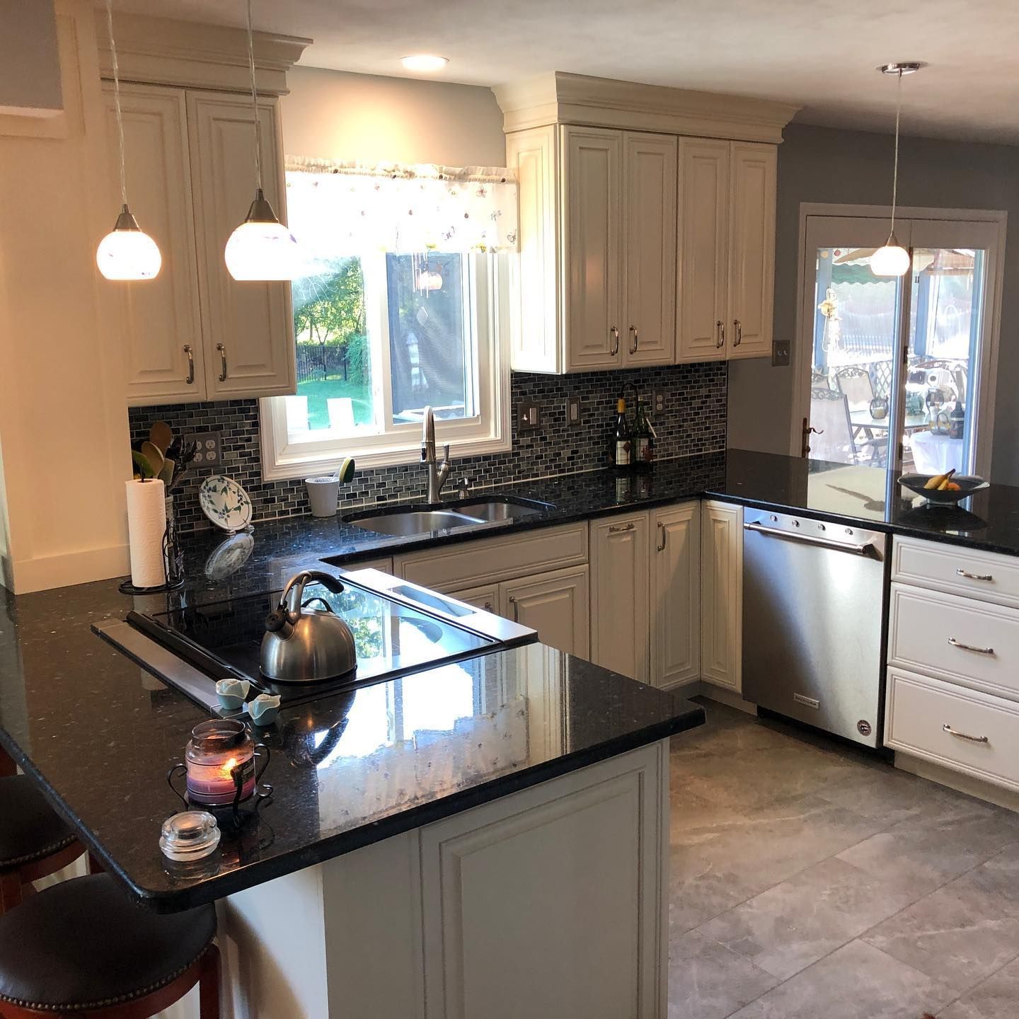 A kitchen with white cabinets , black counter tops , stainless steel appliances and a large island.