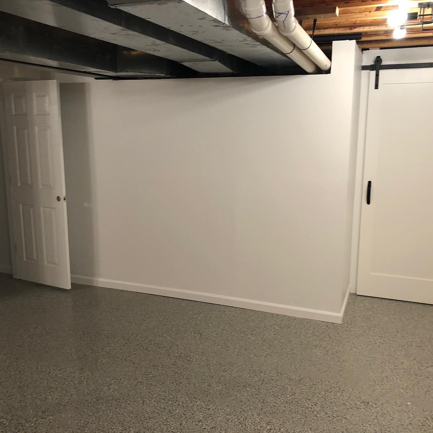 An empty basement with a sliding barn door and white walls.