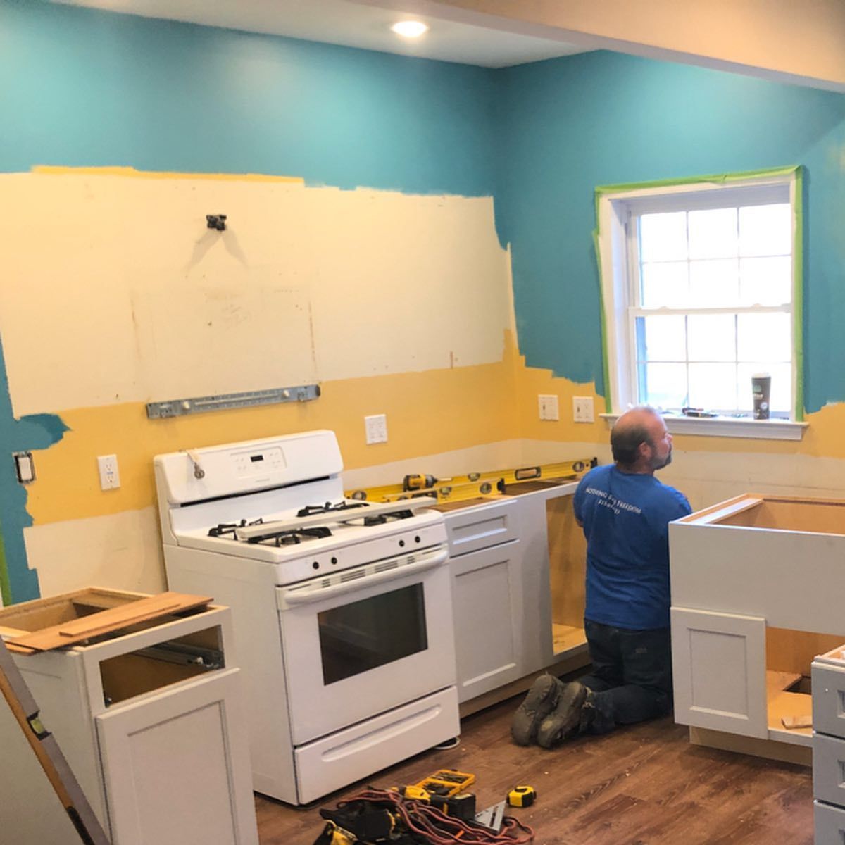 A man is kneeling in a kitchen while working on a stove.