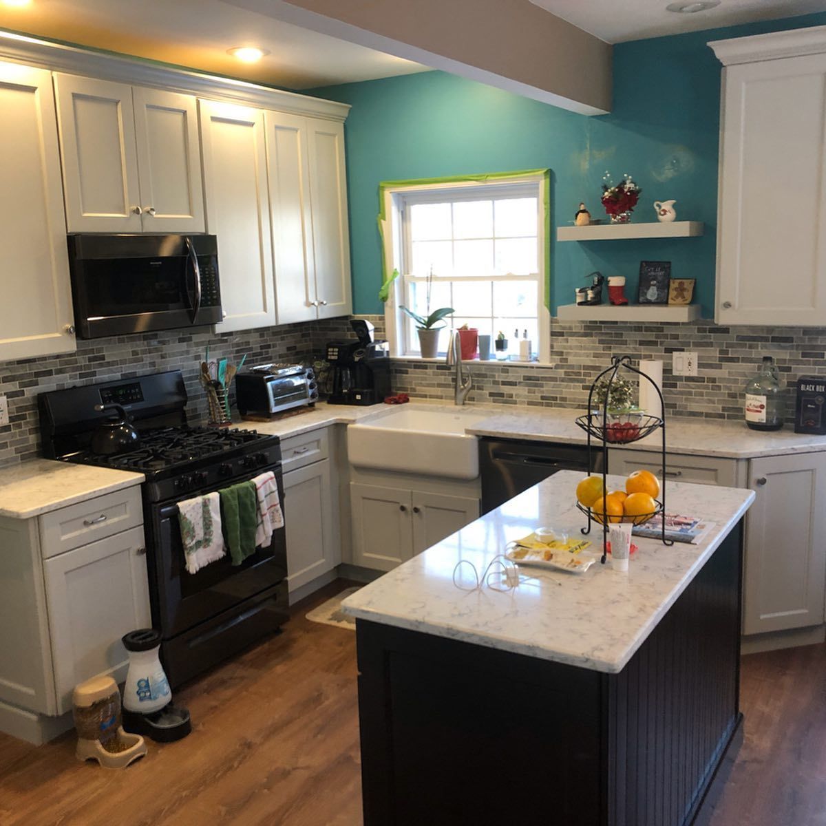 A kitchen with white cabinets , a stove , a sink , and a large island.