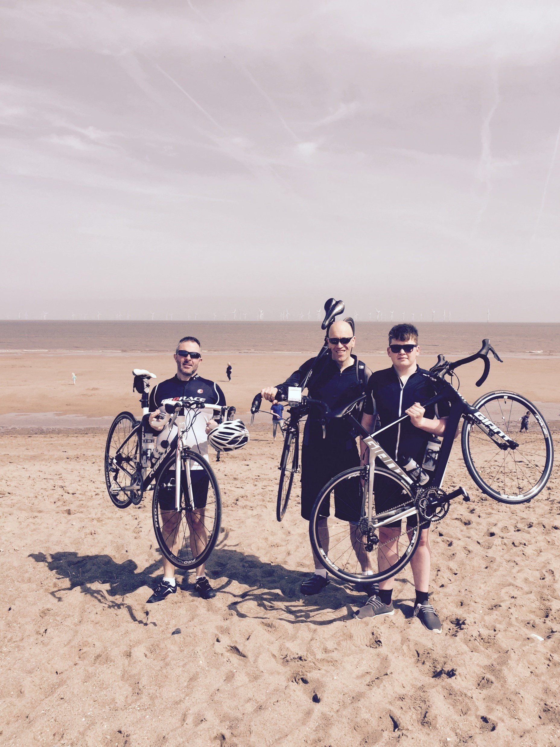 Three people holding bikes on a sandy beach