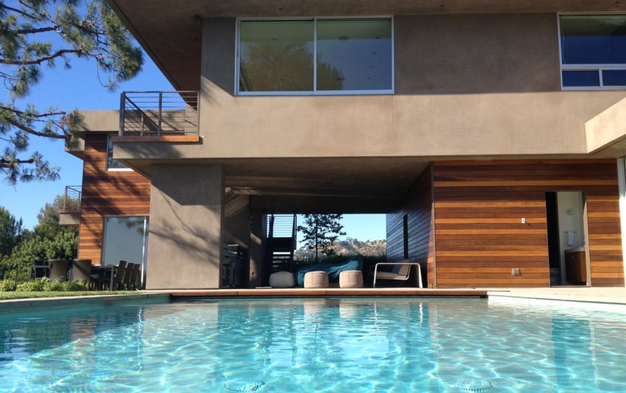 Pool with view of modern two-story home with wooden accents and windows. Sunny, blue water.