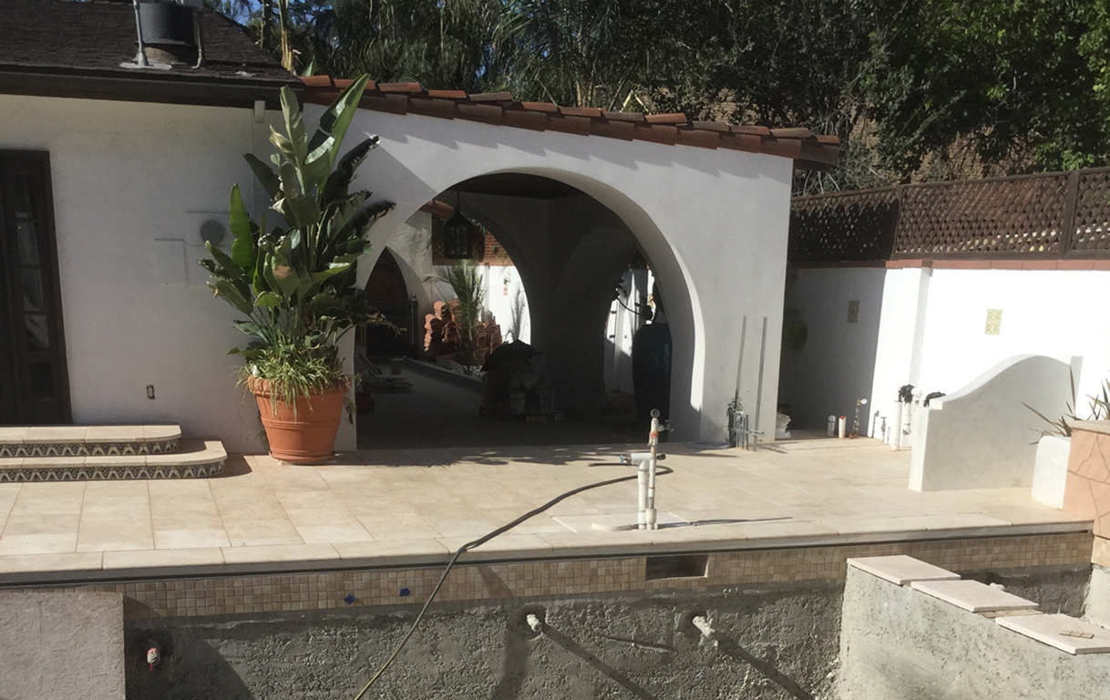 White stucco arches on a patio, overlooking a partially constructed pool, with a potted plant.
