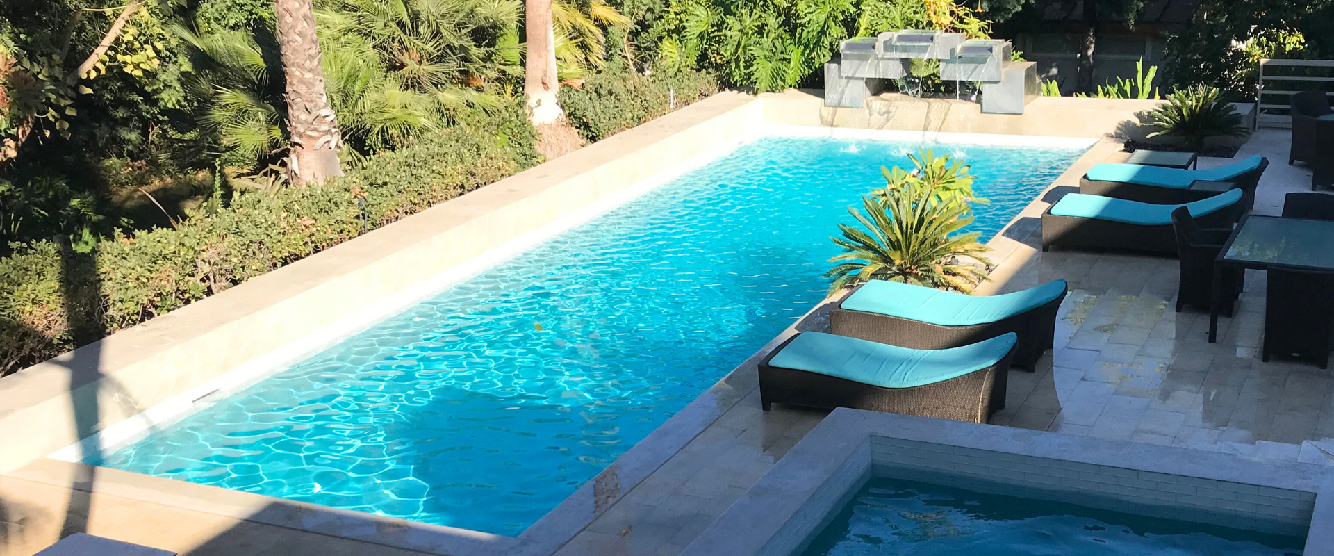 A rectangular outdoor pool with turquoise water, lounge chairs, and a small jacuzzi. Green foliage surrounds the area.