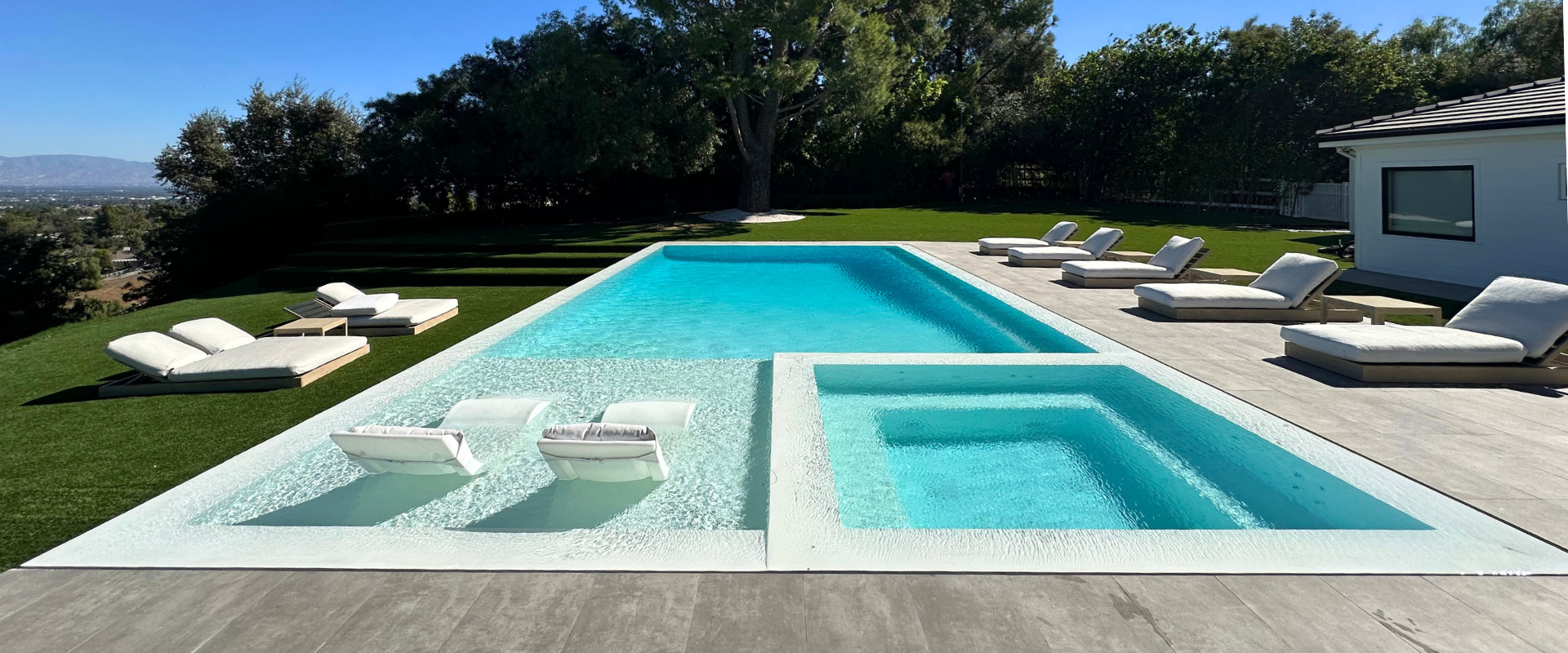 A modern pool with integrated jacuzzi, surrounded by lounge chairs, on a sunny day.
