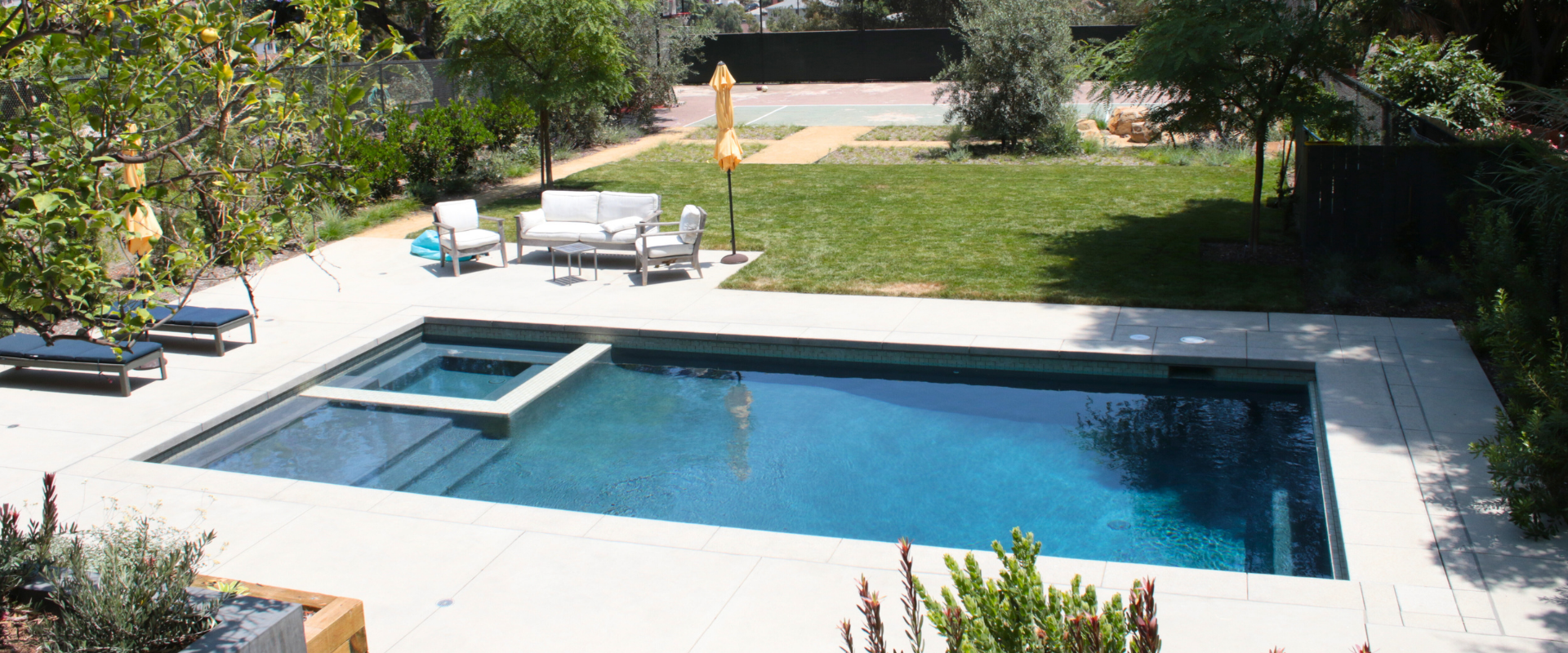 Swimming pool with white deck and furniture in an outdoor setting.