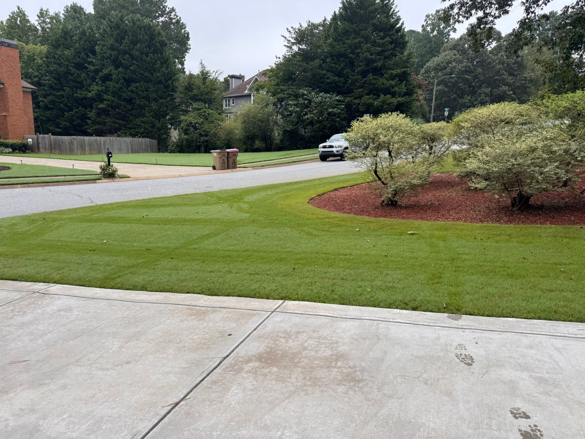 A large lawn with trees in the background and a house in the background.