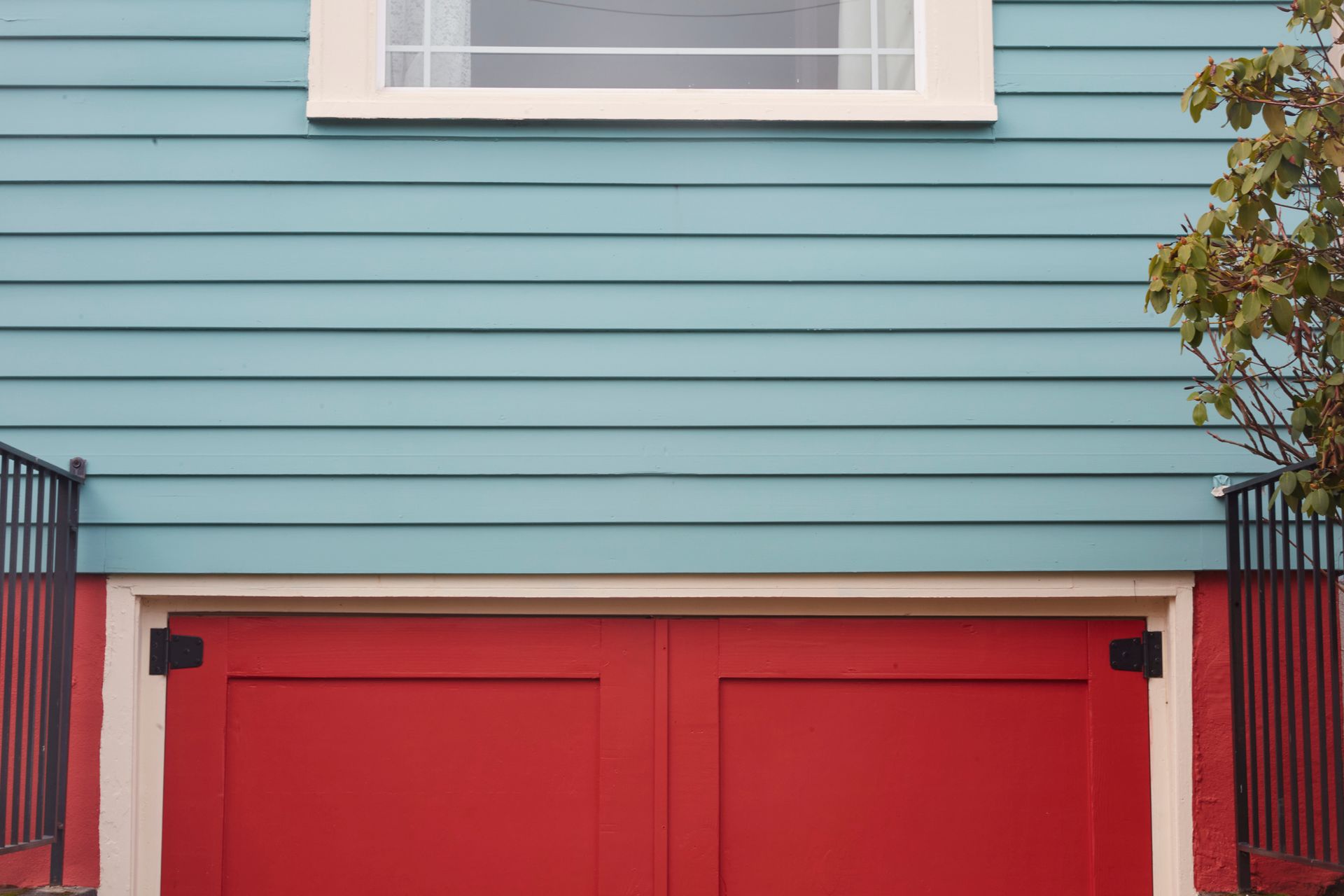 A blue house with a red garage door and a window.