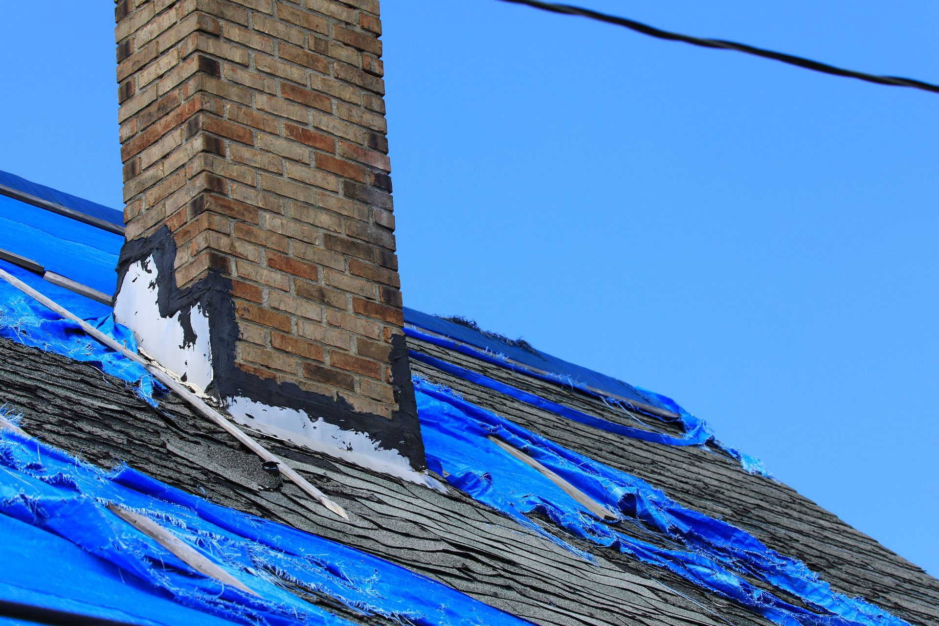 A brick chimney is sitting on top of a roof covered in blue tarps.