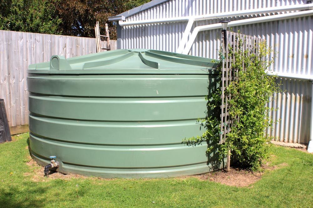 A Green Water Tank Is Sitting In The Grass In Front Of A Building — NSL Plumbing and Gas in Banora Point, NSW