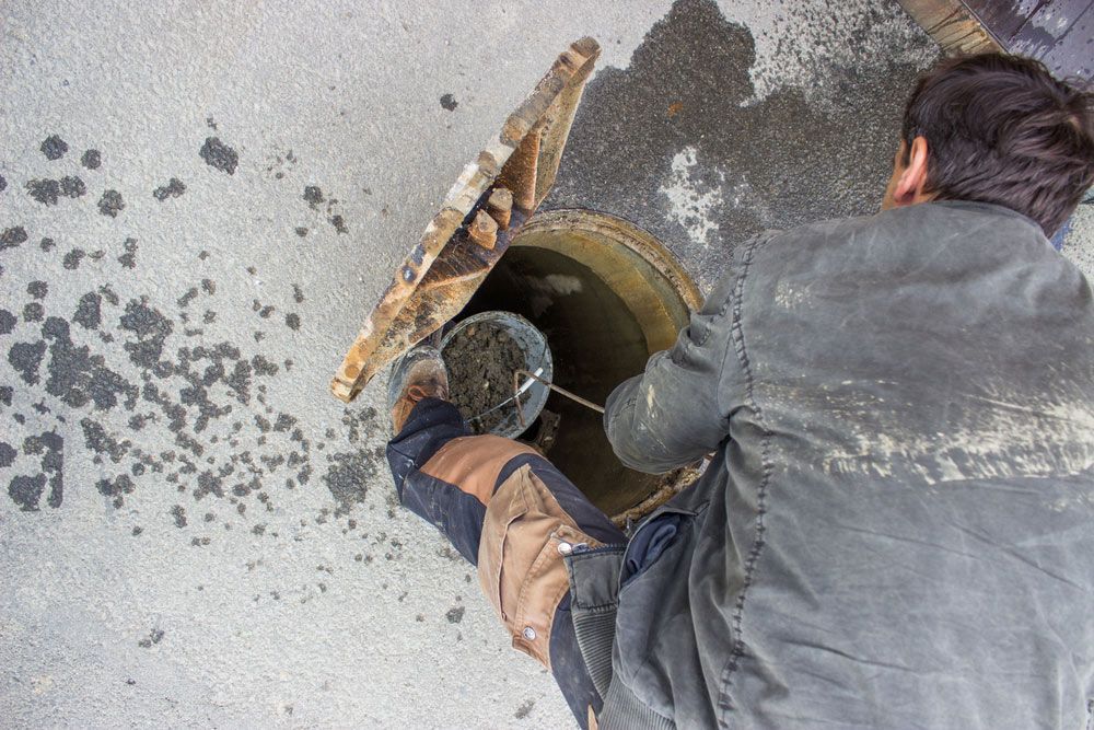 A Man Is Cleaning A Manhole Cover With A Bucket — NSL Plumbing and Gas in Banora Point, NSW