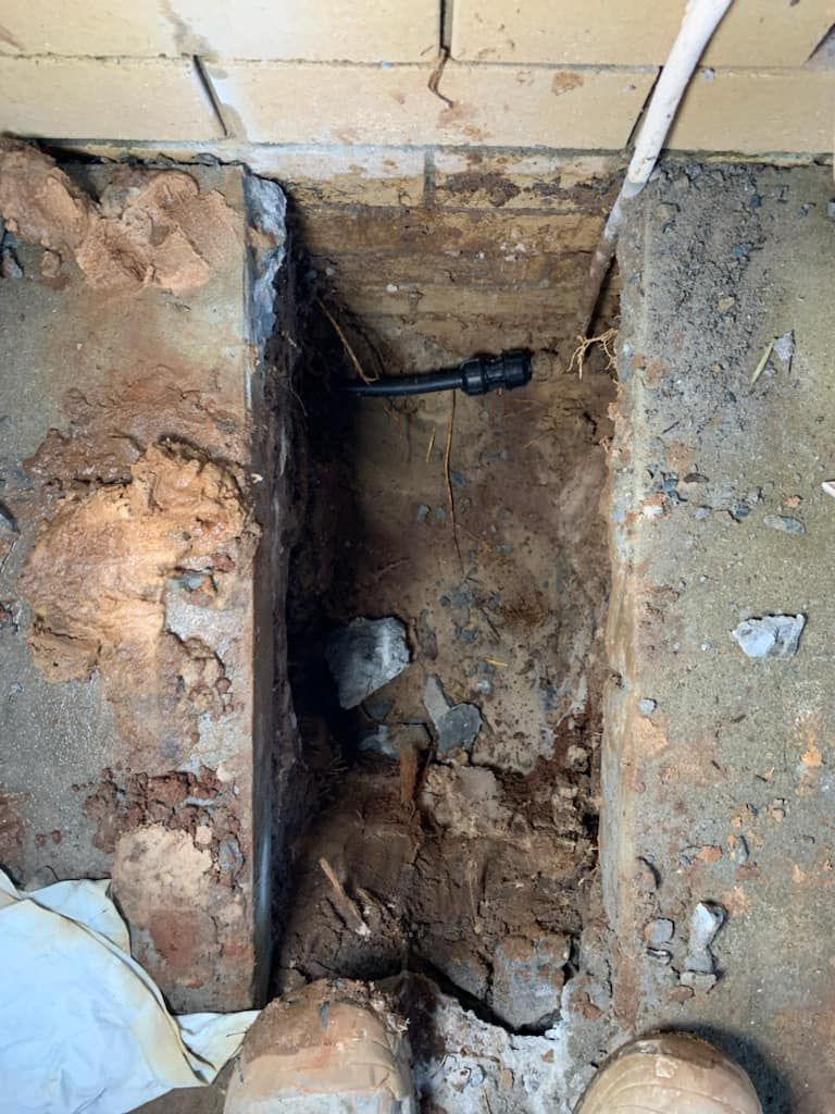A Person Is Standing In A Hole In The Ground Next To A Brick Wall — NSL Plumbing and Gas in Banora Point, NSW