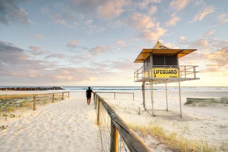 A Man Is Walking Towards A Lifeguard Tower On A Beach — NSL Plumbing and Gas in Coolangatta, NSW