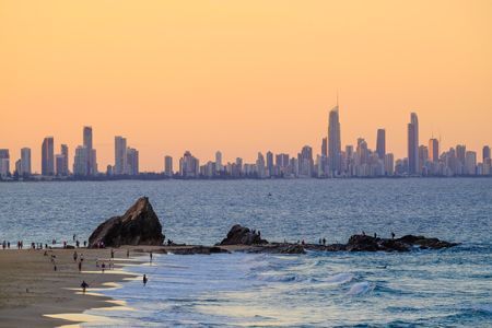 A Beach With A City Skyline In The Background And A Large Rock In The Foreground — NSL Plumbing and Gas in Currumbin, NSW