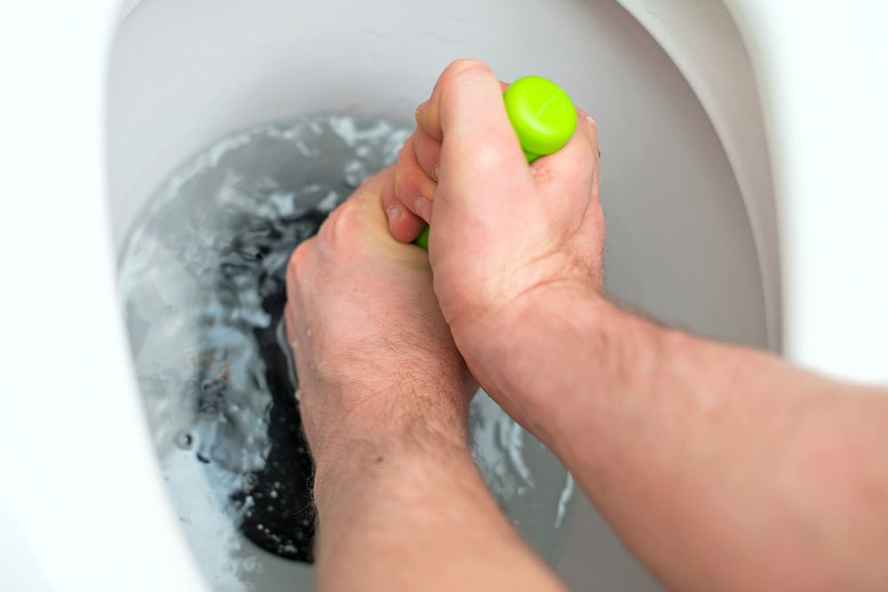 A Man Is Using A Green Plunger To Unblock A Toilet — NSL Plumbing and Gas in Coolangatta, NSW