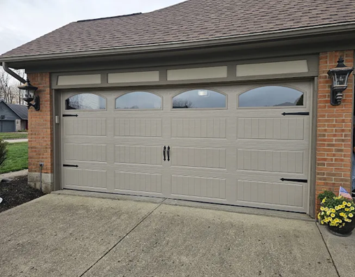 Tan garage door with arched windows and black hardware on brick house. Tan garage door with arched windows and black hardware on brick house.