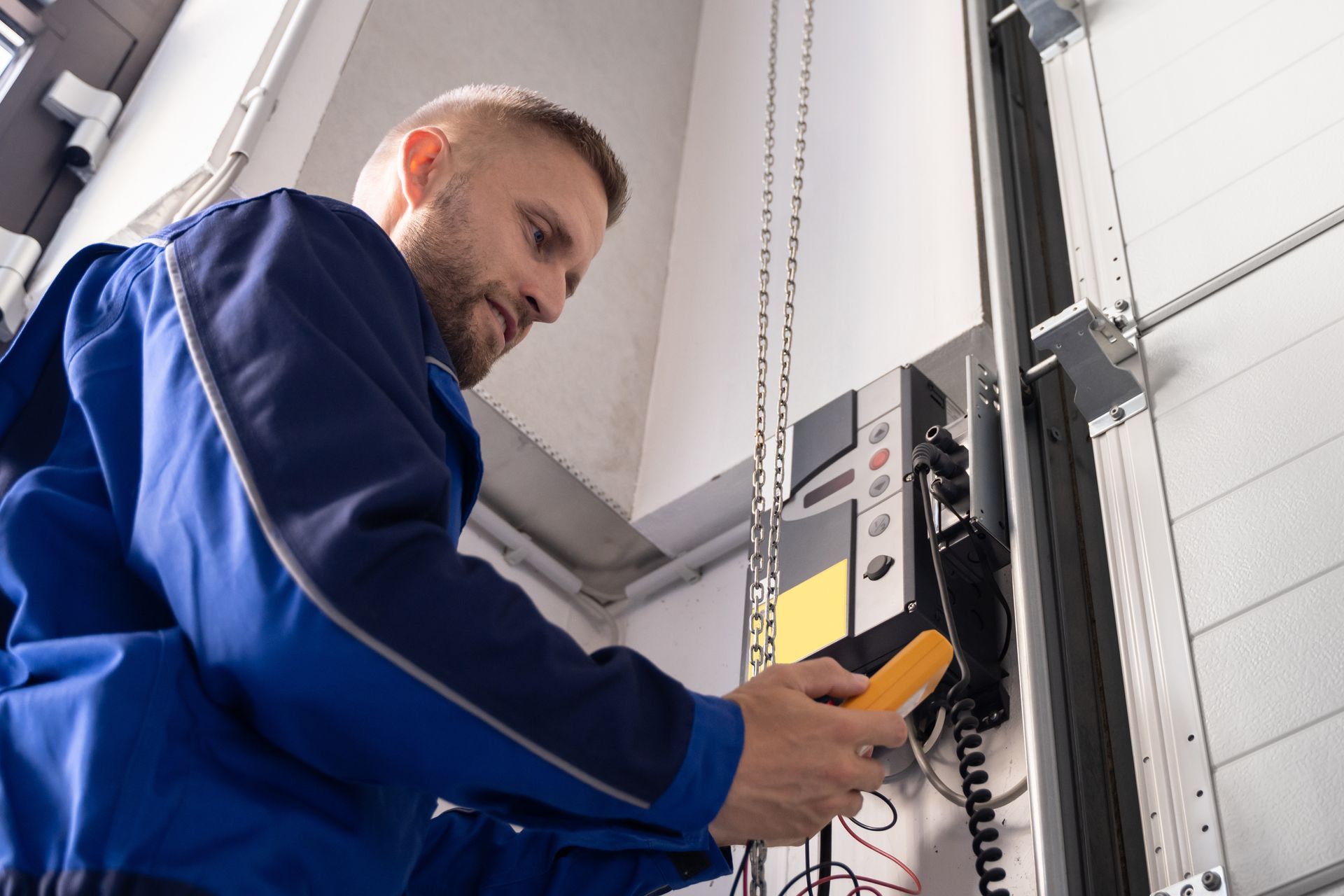 Technician testing a garage door motor with a handheld meter inside a garage.