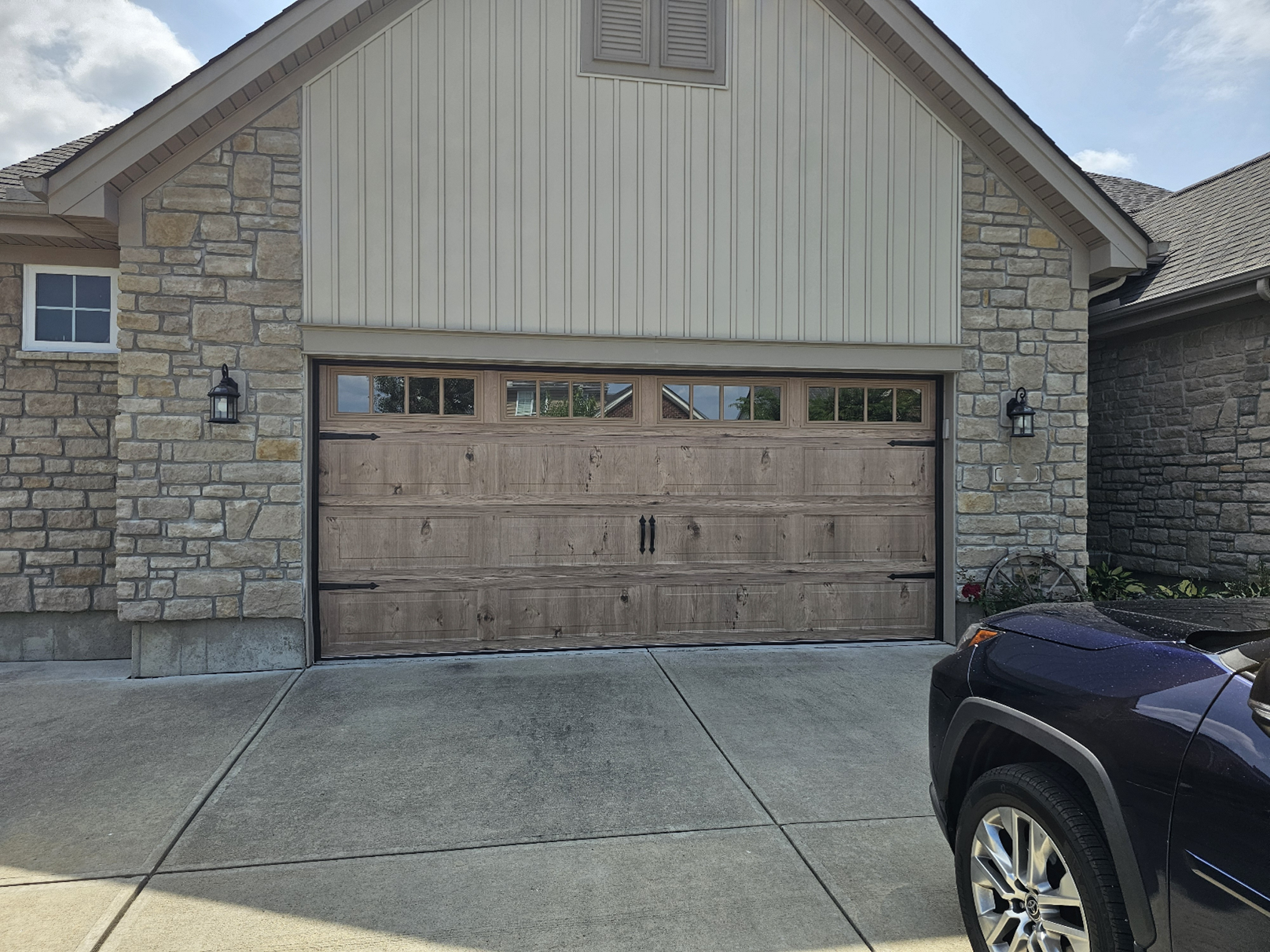 Garage with wood door and stone facade. A vehicle is partially visible in the foreground. Garage with wood door and stone facade. A vehicle is partially visible in the foreground.