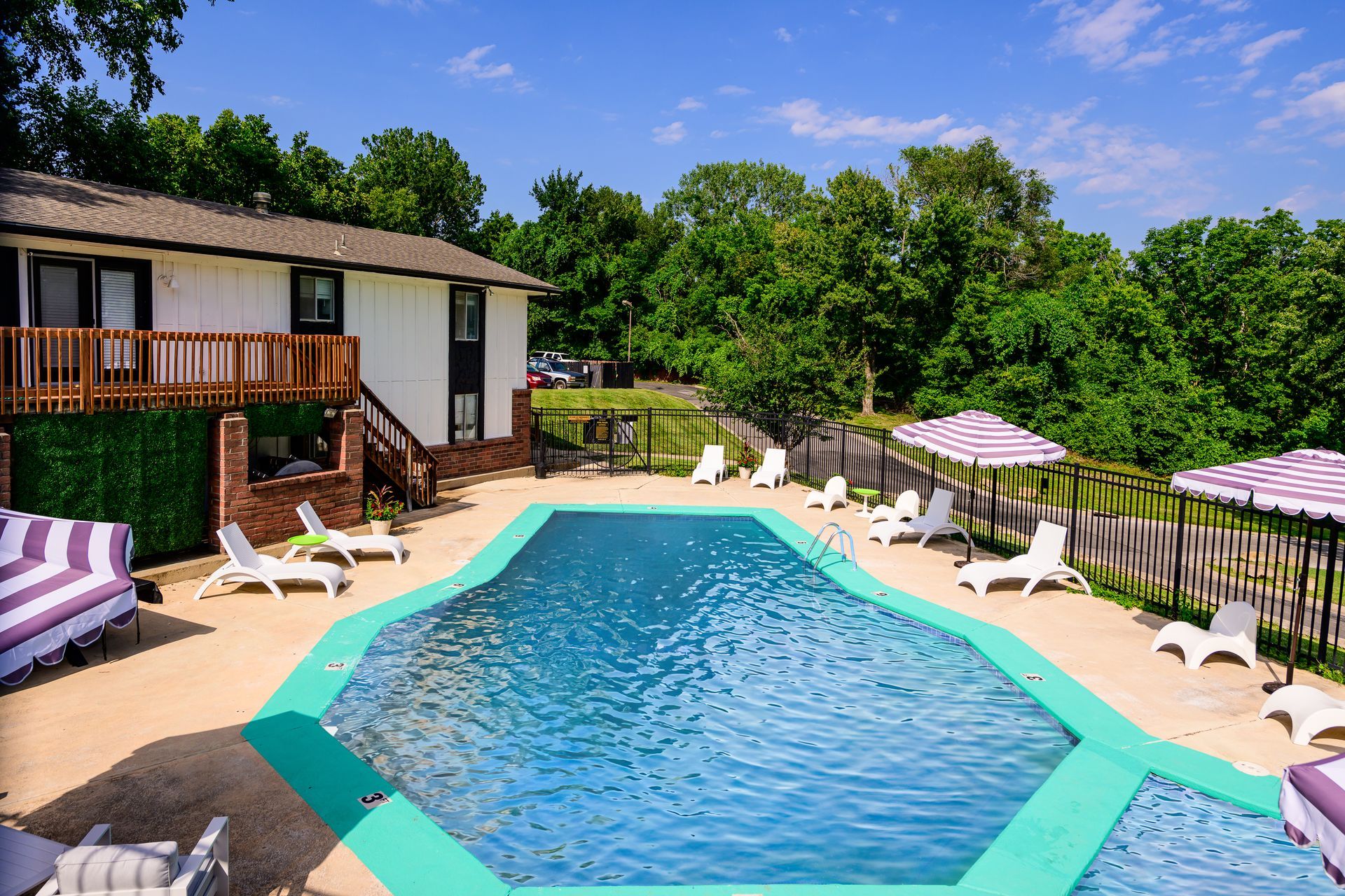 A large swimming pool surrounded by chairs and umbrellas in front of a house.