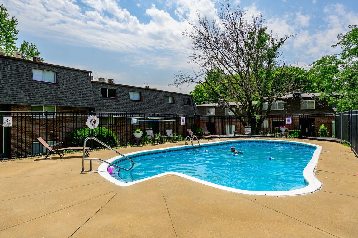 A large swimming pool is surrounded by a fence in front of a building.